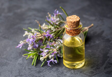 Rosemary Oil. Rosemary Essential Oil Jar Glass Bottle And Branches Of Plant Rosemary With Flowers On Rustic Background.