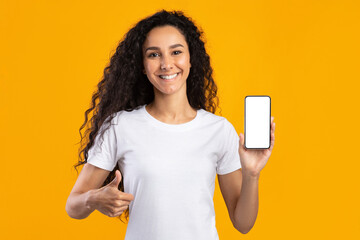 Woman Showing Cellphone Empty Screen Gesturing Thumbs Up, Yellow Background