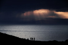 Four People Backlit In An Oceanfront Sunset Scene. Sunbeams Break Through The Clouds At Sunset. Cabo De Gata Park. Almeria