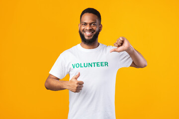 Smiling african volunteer man pointing thumbs at himself, yellow background
