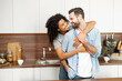 © Vadim Pastuh - Close-up of a happy interracial couple standing in the kitchen, happy romantic owners of a new flat smiling and looking at each other, young African American woman hugging handsome man from behind