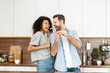 © Vadim Pastuh - Happy interracial couple dancing in the kitchen, singing while cooking breakfast or dinner, young African American woman and a handsome man smiling and having fun together, holding kitchen utensils