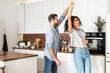 © Vadim Pastuh - Handsome white man and attractive African American young woman is cooking and having fun together while cooking on the kitchen, romantic interracial couple is dancing while preparing lunch or dinner