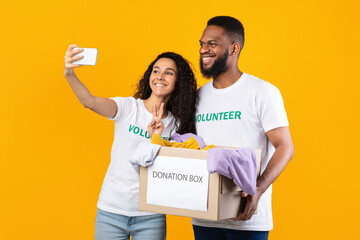 Wall Mural - Two Volunteers Making Selfie With Donation Box Over Yellow Background