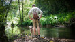 © Darío Peña - Hombre joven con mochila de piel y pantalón corto junto a río en bosque de Asturias con su perro pastor catalán beige