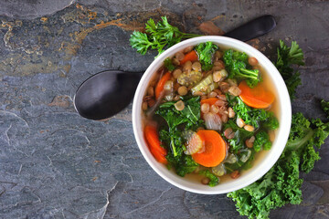 Wall Mural - Healthy vegetable soup with kale and lentils. Top view scene on a dark slate background.