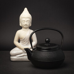 Tea ceremony. Teapot and buddha on black table.