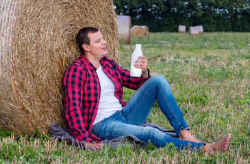 man drinks fresh bio milk on the field in the background, hay, grass, farm