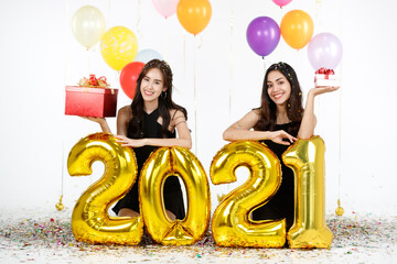 Two young and beautiful sexy Asian girls holding golden numeric 2021  balloons with funds and happiness. Idea for new year celebrate party