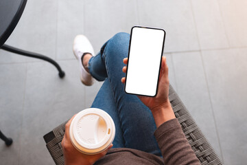 Wall Mural - Top view mockup image of a woman holding mobile phone with blank white desktop screen while drinking coffee