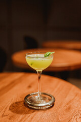 Wall Mural - A sour cocktail in a coupe glass with a basil leaf garnish. Lifestyle vertical image. Selective focus.