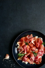 Wall Mural - Slices of prosciutto di parma or jamon serrano (iberico)  on a black plate. Top view with copy space.