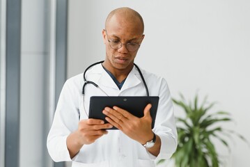 Wall Mural - Mature african doctor using digital tablet in corridor . Portrait of confident male doctor using tablet computer in clinic with copy space. Successful smiling doctor in labcoat wearing stethoscope.