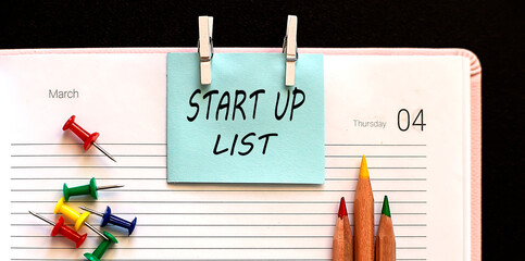 Poster - text START UP LIST on the stickers on the diary with office tools