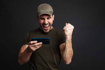 Wall Mural - Excited masculine military man playing online game on mobile phone