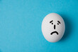 © queen1987 - An egg with a sad face. Isolate on a blue background.