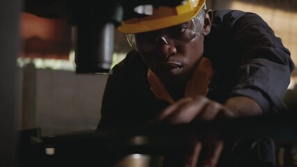 Wall Mural - American industrial black young worker man with yellow helmet and ear protection surveillance for examination in front machine, Engineer inspection checking work in the industry factory.