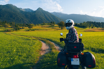 Man motorcyclist ride touring motorcycle. Alpine mountains on background. Biker lifestyle, world traveler. Summer sunny sunset day. Green hills. hermetic packaging bags. copy space. Slovenia