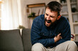 © JustLife - Sick man at home. Young man sitting on sofa having fever