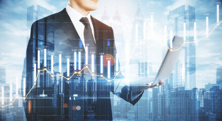 Wall Mural - Business analytics concept with businessman following the process by laptop at city background and digital screen with infographic column diagram. Double exposure.