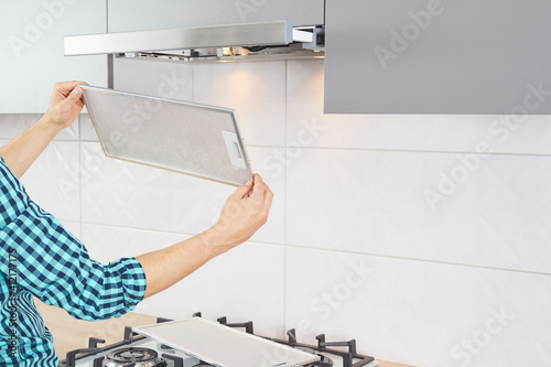 Mans hands removing a filter from cooker hood for cleaning or service. Replacing filter in kitchen hood. Modern kitchen fan or range hood.