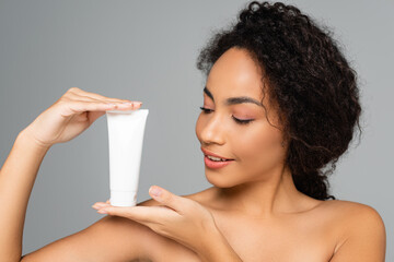 Wall Mural - Smiling african american woman positing with tube of cleansing foam isolated on grey