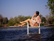 © NaturyStocker - A woman sitting in a chair in the middle of the river