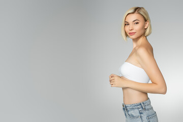 Wall Mural - Blonde woman in white top looking at camera isolated on grey