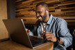 © shunevich - Friendly African American using a laptop, looking at the screen, chatting with colleagues on a social network, reading good news via email. Business young man negotiates a working plan.