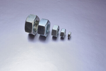 five new chrome nuts of different sizes from large to small are lined up. metallic background. close-up.