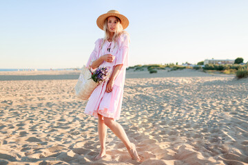 full height image of blond girl in cute pink dress dancing and having fu on the beach. holding straw