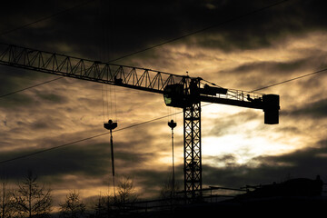 A tall construction crane against the setting sun. Machine for high-altitude lifting of building materials.