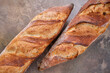 Two freshly baked baguettes on a stone background.