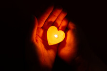 Woman Hands Holding A Candle In The Form Of A Heart On A Black Background. Charity And Giving Back.  Faith, Charity, Sacrifice, Religion Concept. Save A Life. Candle Light Glowing In Woman's Hand. 