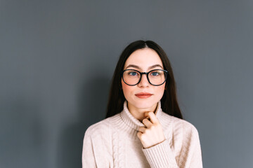 Wall Mural - Portrait of smiling young caucasian woman in eyeglasses on gray background looking at camera.