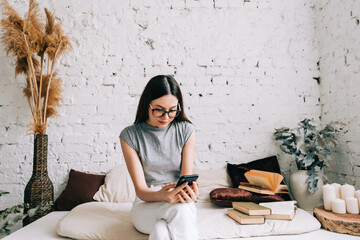 Young caucasian woman in eyeglasses using mobile phone while resting on a sofa at home. 