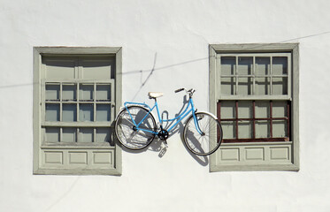 Retro bicycle on exterior wall of cement facade. Two old closed sash windows on white facade and hanging bicycle. Decorative bicycle hanging on the white wall. Original decoration of building exterior