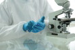 © Qwenergy - Doctor in protective suit goggles straightens blue gloves near microscope in medical laboratory