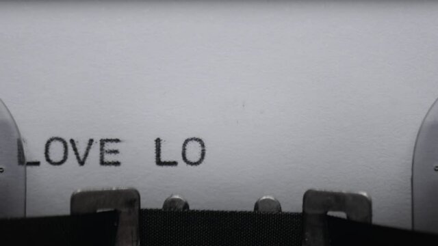 Typing text LOVE on vintage manual typewriter. Close up of writes words on white paper. Shot in macro. Loop video. Concept of Valentine's Day.