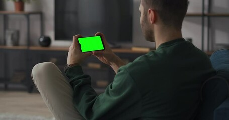 adult man is using smartphone with green screen for chroma key, online chat concept, holding gadget horizontally