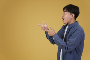 portrait of handsome young asian man dressed casually pointing fingers at copyspace. yellow background