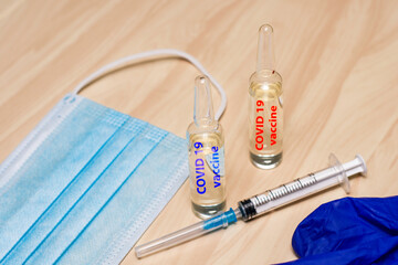 Wall Mural - a syringe mask gloves and ampoules labeled covid19 vaccine in blue and red are on the table