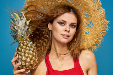 A woman in a straw hat with a pineapple in her hands or is it a fun blue exotic fruits background