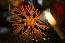 Light Bulb On The Christmas Tree Illuminating A Rustic Straw Toy In The Shape Of A Snowflake