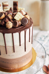 Poster - Vertical shot of chocolate ombre naked cake with sweets and chocolate drip on glass cake stand