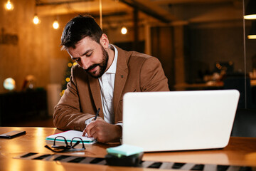 Wall Mural - Young businessman using laptop in his office. Businessman taking a notes while working on laptop.