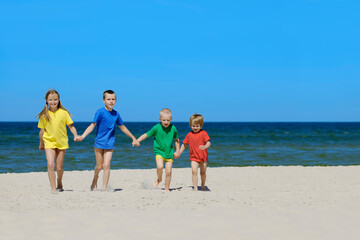 Wall Mural - Two girls and two boys in colorful t-shirts walking on a sandy beach