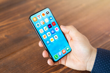 Man holding in hand mobile phone with different everyday application icons on home screen