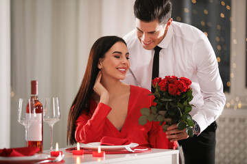 Wall Mural - Man presenting roses to his beloved woman in restaurant. Romantic Valentine's day dinner