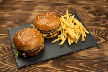 Two gourmet delicious burgers with french fries slices on a black board on a wooden background. Fast food